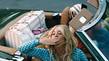 Woman sitting in a boat with luggage around her, wearing a blue checkered shirt.