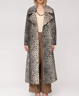 A model stands against a light gray studio background wearing a long leopard-print coat over a cream top and brown wide-leg pants.