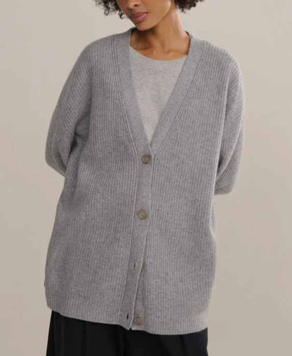 Person wearing a gray cardigan over a light gray shirt on a beige background