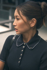 Woman wearing a dark blue outfit with a high collar, standing indoors.