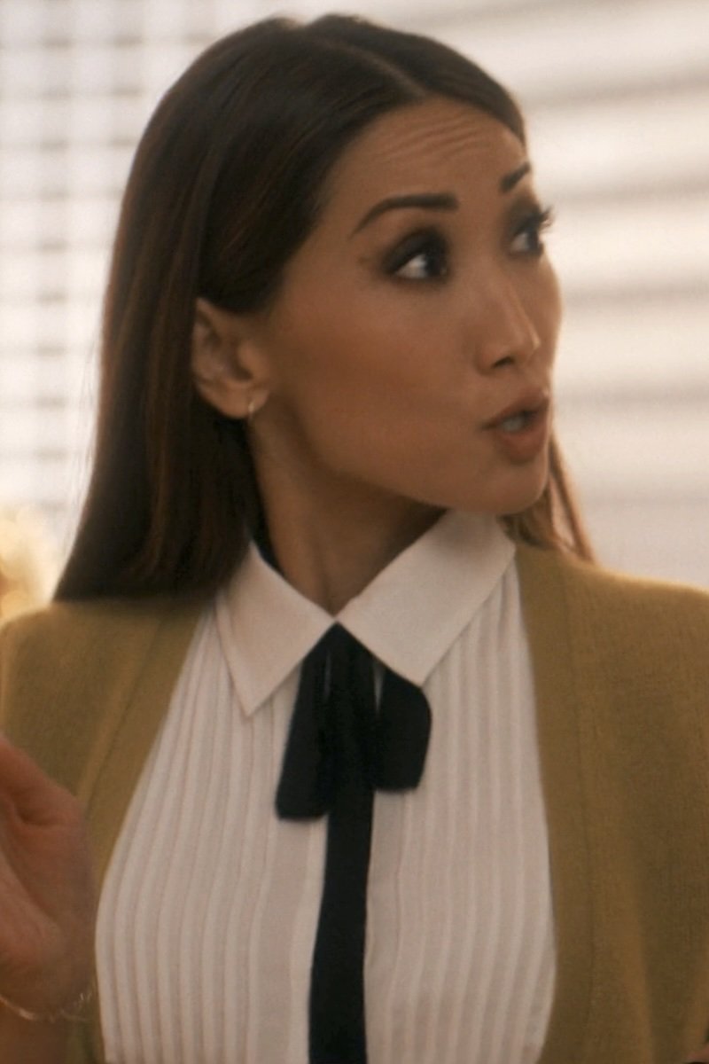 Woman wearing a mustard cardigan over a white shirt with a black tie, indoors.