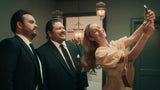 Woman taking a selfie with two men in formal attire in an indoor setting.
