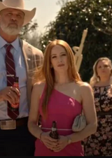 Woman in a pink dress holding a beer bottle, standing next to a man in a cowboy hat.