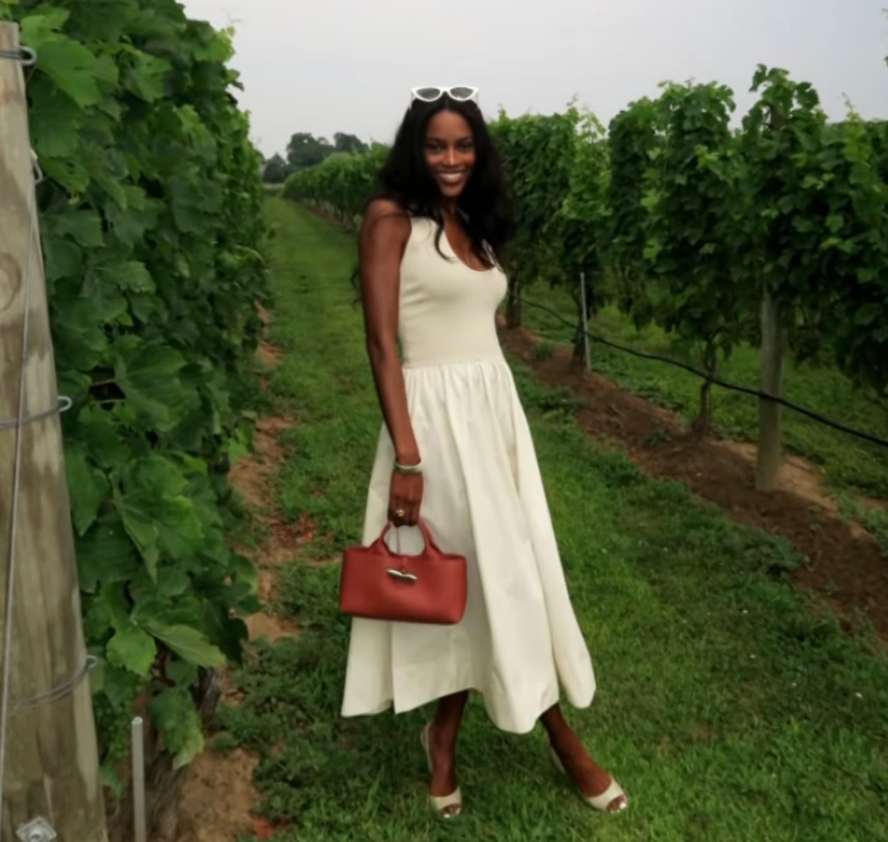 Woman in a white dress holding a red handbag in a vineyard
