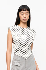 Woman wearing a sleeveless polka dot top and gray pants on a white background