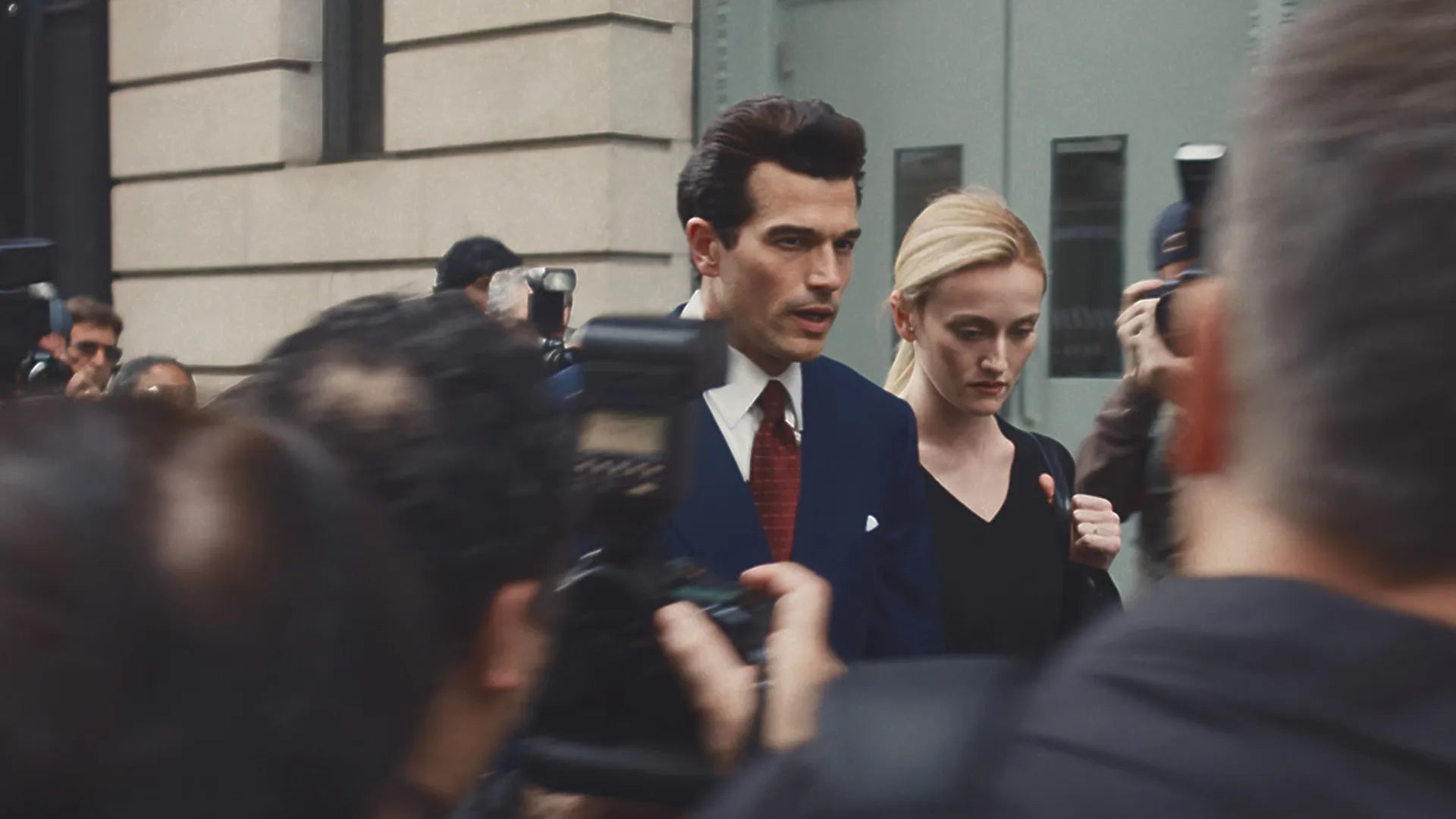 Man and woman walking through a crowd of photographers and onlookers.