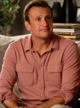 Man wearing a pink shirt sitting on a couch with a blurred background