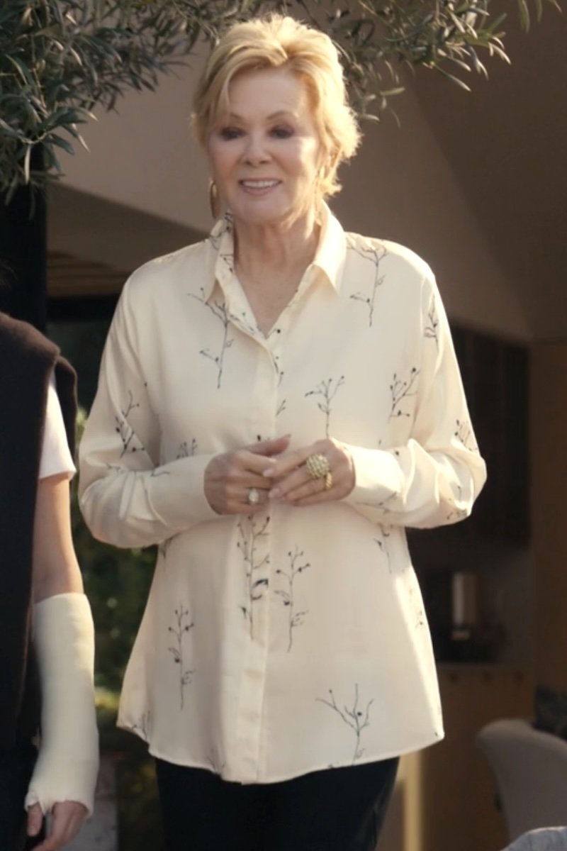A woman wearing a cream-colored long-sleeve button-up shirt with a delicate black botanical branch print, standing in an outdoor setting.