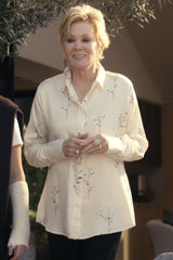A woman wearing a cream-colored long-sleeve button-up shirt with a delicate black botanical branch print, standing in an outdoor setting.