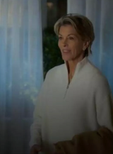 Woman in a white outfit standing in a softly lit room with curtains.