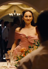 Woman in a pink dress sitting at a table with floral decorations in a formal setting.