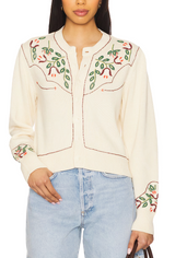 Woman wearing a cream-colored embroidered blouse with floral patterns and light blue jeans.