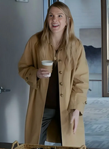 Woman in a beige coat holding a coffee cup in a room with a door and wall art.