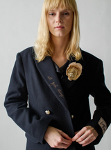 Woman wearing a dark blue coat with floral brooches on a plain background