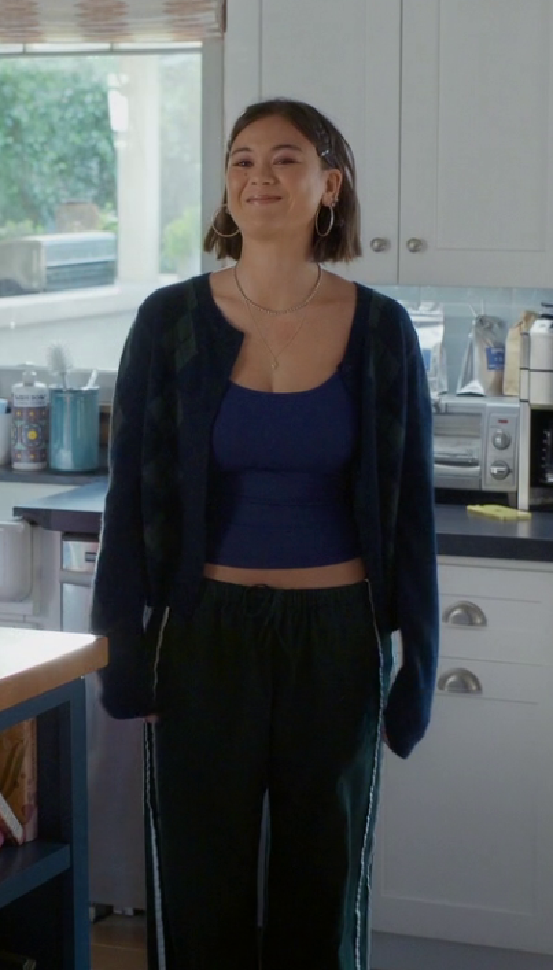Woman standing in a kitchen wearing a dark blue top and black cardigan.