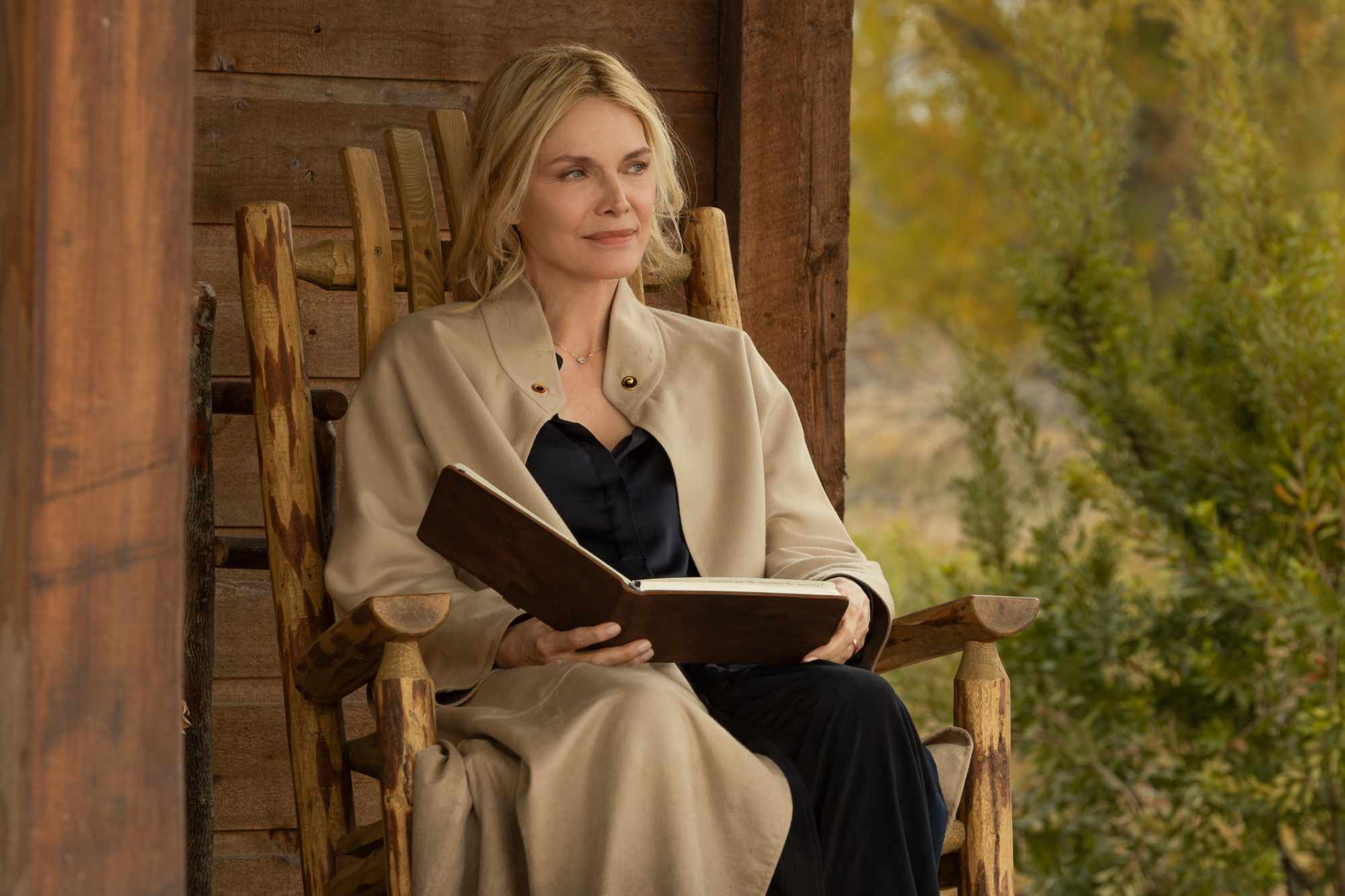 Woman sitting in a wooden chair reading a book outdoors.