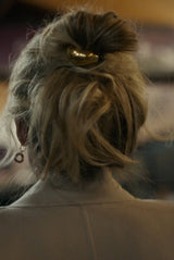 Close-up of a person's hair styled in an updo with a gold hair accessory, wearing a beige coat.