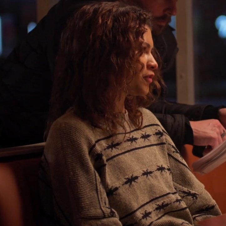 Person wearing a patterned sweater sitting next to another person in a dimly lit setting