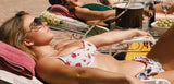 Woman in a floral bikini sunbathing on a lounge chair with a poolside setting.