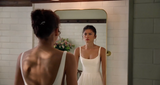 Woman in a white dress standing in front of a mirror in a bathroom.