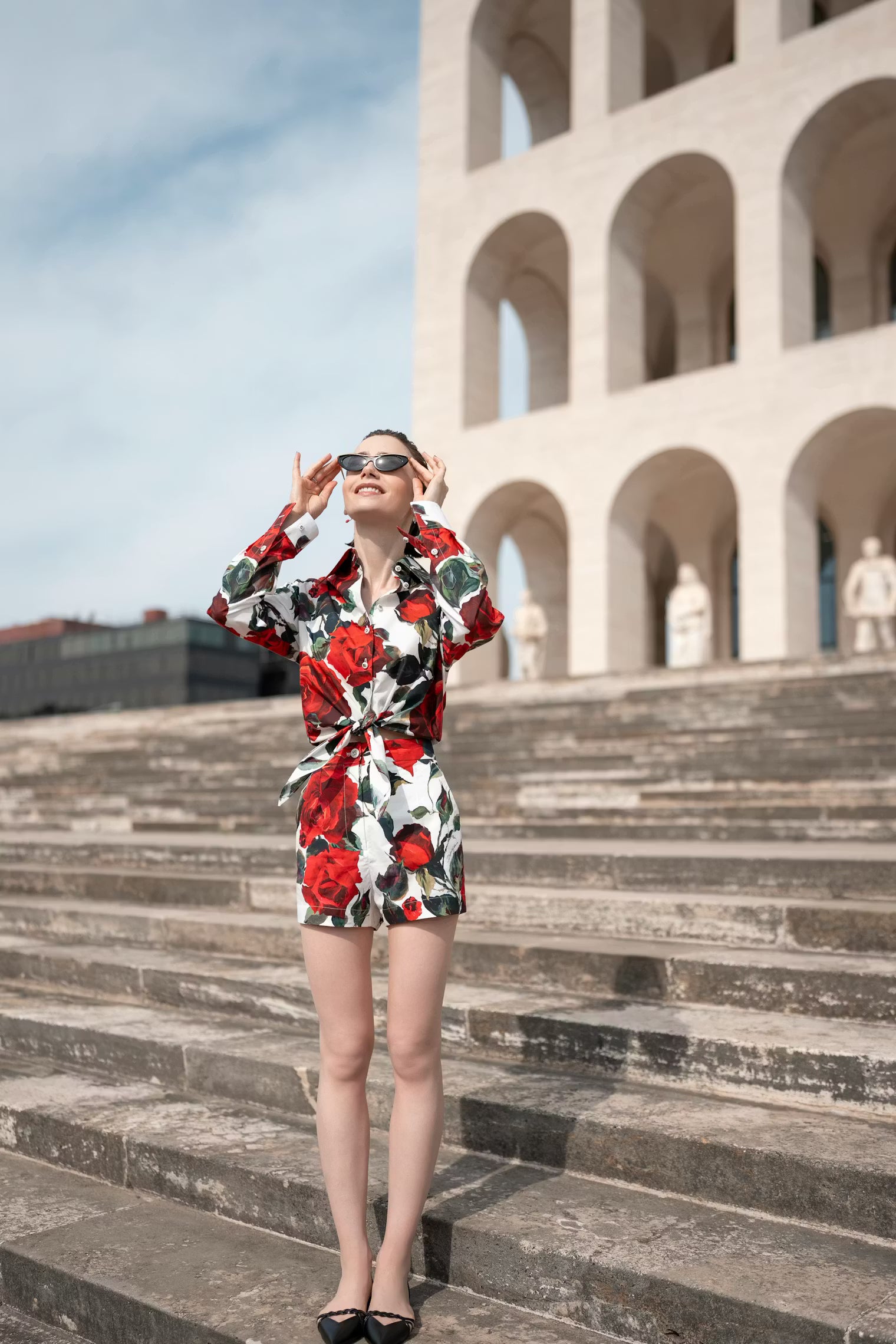 Woman in a floral dress standing on stone steps with a building in the background