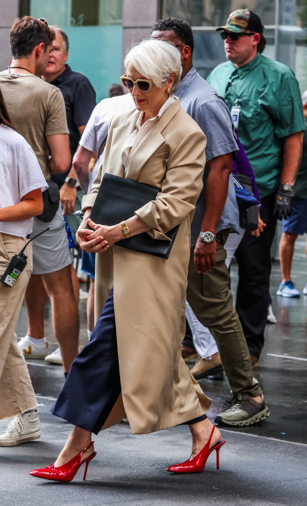 Woman in a beige coat and red high heels walking on a busy street.