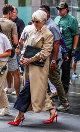 Woman in a beige coat and red high heels walking on a busy street.