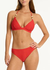 A woman modeling a red two-piece bikini with small gold ring accents on the halter straps, standing against a plain white studio background.